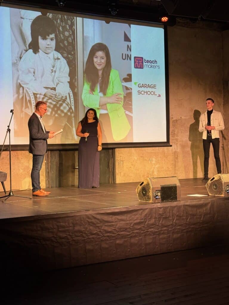 Žena na pódiu během slavnostního ceremoniálu s prezentací a logy Teach Makers a Garage School.