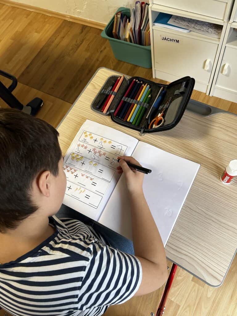 Školák kreslí na papír s barvami a fixami, učení a kreativní práce v domácím prostředí.