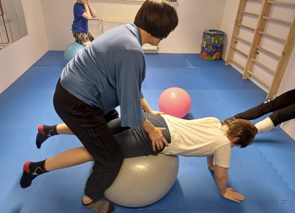 Pomoc při rehabilitaci s cvičením na velkém míči v terapeutickém prostředí.